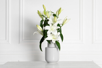 Beautiful bouquet of lily flowers in vase on light table near white wall
