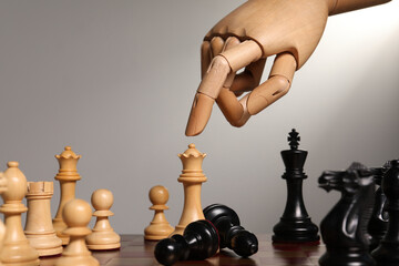 Robot moving chess piece on board against light grey background, closeup. Wooden hand representing...