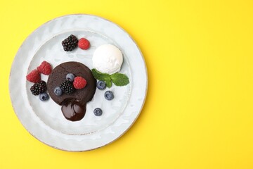 Fototapeta premium Delicious chocolate fondant served with fresh berries and ice cream on yellow background, top view. Space for text