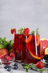 Delicious refreshing sangria with fresh fruits and berries on light grey table, space for text