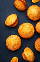 Sweet muffins with oranges and candied fruit on black table background, homemade pastries, top view