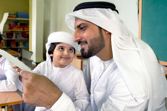 Arab parent father checking his son's school grades with a black green board as background. Arabic father and kid holding paper ideal for learning homework or exam results.