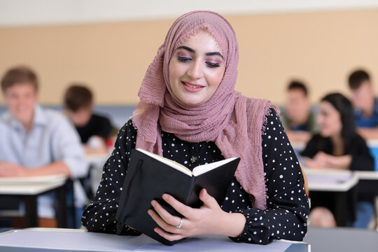 Female college student wearing Hijab Shayla head scarf inside a classroom University ideal for Middle Eastern concept Saudi, Emirati, Qatari, Omani girl at school reading notebook.