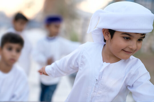 Arab student at school with classmates on the background wearing traditional Kandura Dish dasha for Emirati, Saudi, Qatar, Oman, Kuwait or Bahrain education concept. Happy Arabic boy.