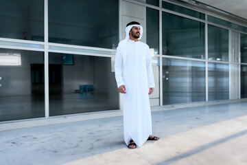 Standing full portrait of Arab Emirati man at a business center with empty shops as background