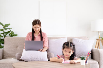 Working mom works from home office. Happy mother and daughter look to each other. Woman and cute child using laptop. Freelancer workplace in cozy kitchen. Female business, kindness, care. Lifestyle.