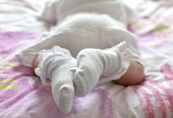 baby in white clothes lies on his stomach on the bed