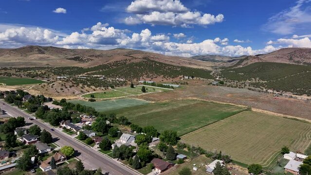 Aerial rural city farms cemetery climb fast motion. Farming community agricultural economy. Spring summer weather mountain valley green agriculture field. Homes, barns and buildings.
