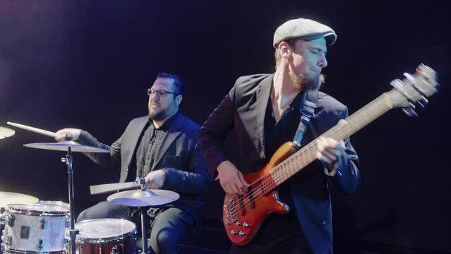 Musicians playing drum set and guitar with band. Handheld shot of drummer and guitarist performing together on stage. Performers having fun in rock concert. 