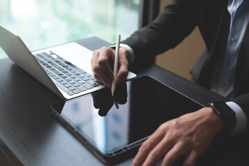 Closeup of businessman using stylus pen signing e-document on digital tablet and working on laptop...