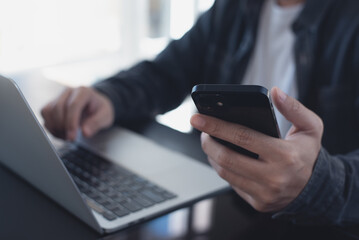 Casual business man, freelancer using mobile phone and online working on laptop computer on table, searching the information, internet networking at home office, close up