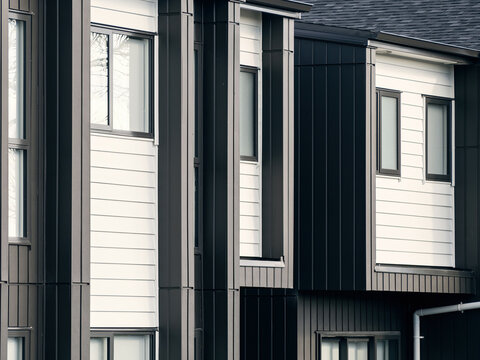 Close-up of row of attached modern newly built two storeys residential townhouses with windows. Horizontal white and vertical black weatherboards exterior walls design.