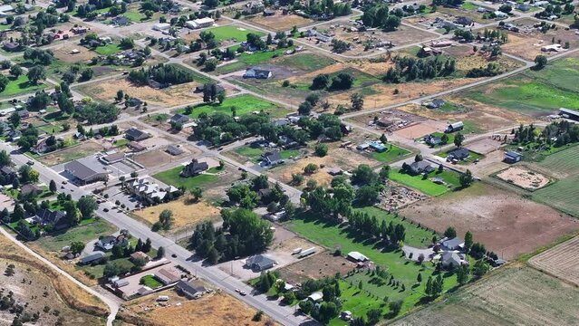 Aerial rural city traffic homes and fields Utah 1. Farming community agricultural economy. Spring summer weather mountain valley green agriculture field. Homes, barns and buildings.
