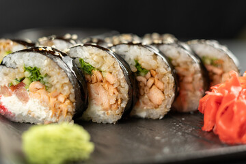 sushi roll futomaki with cucumber and fried salmon on a black stone plate.