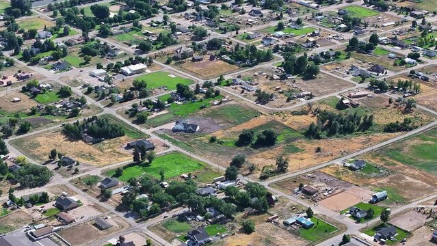 Aerial rural city traffic homes and fields Utah 2. Farming community agricultural economy. Spring summer weather mountain valley green agriculture field. Homes, barns and buildings.