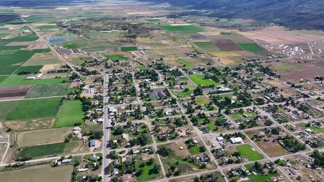 Aerial rural town traffic homes valley fields Utah 1. Farming community agricultural economy. Spring summer weather mountain valley green agriculture field. Homes, barns and buildings.