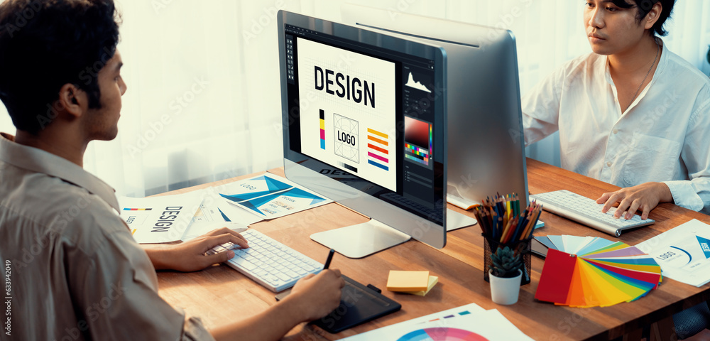 Poster Graphic designer work on computer laptop and with graphic drawing pen while brainstorming unique design with professional graphic team in modern digital studio workplace. Panorama shot. Scrutinize