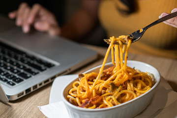 Eating spaghetti while working on laptop at home. Unhealthy food during conference call, meeting.