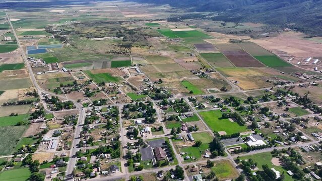 Aerial rural town traffic homes valley fields Utah 2. Farming community agricultural economy. Spring summer weather mountain valley green agriculture field. Homes, barns and buildings.
