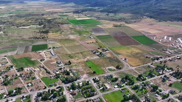 Aerial rural town traffic homes valley fields Utah 3. Farming community agricultural economy. Spring summer weather mountain valley green agriculture field. Homes, barns and buildings.