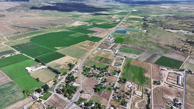 Aerial rural town traffic valley agriculture fields Utah 1. Farming community agricultural economy. Spring summer weather mountain valley green agriculture field. Homes, barns and buildings.