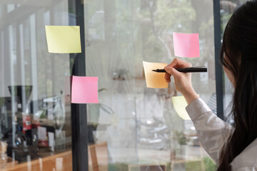 Close up hand businesswoman writing sticky notes on glass wall in office