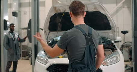 two diverse international auto mechanics, masters working underneath car lifting machine at the garage. Auto repair shop, Car service, repair. black man stands at the car lift in the service station