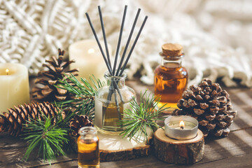 Obraz na płótnie Canvas Assortment of natural Christmas essential oils in small bottles. Candles, branches of fir tree, home aroma diffuser. Aromatherapy, cozy atmosphere, holiday festive mood. Close up macro, wooden table