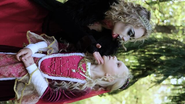 A woman in the form of a vampire or a sorceress poses in the forest with a girl in fairy-tale makeup and medieval dress. Image for Halloween. Vertical video