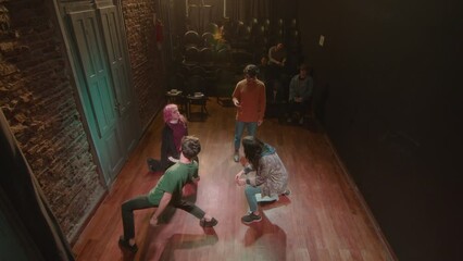 Group of young actors walking on stage and then freezing in a pose while having acting class with a director in a theater. High angle shot