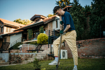 A man digs soil with a shovel in the colorful garden in his yard.