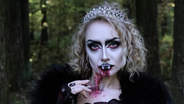 A woman in the image of a vampire or witch with makeup and medieval clothes poses for the camera in the forest. Horizontal video