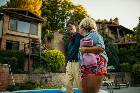 Diverse couple carrying towels and heading for a pool.