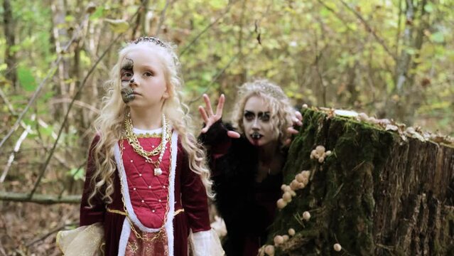 A woman in the form of a vampire or a sorceress is about to bite a princess girl in fairy-tale makeup and medieval dress. The witch is watching the girl. Image for Halloween. Mother and daughter. 