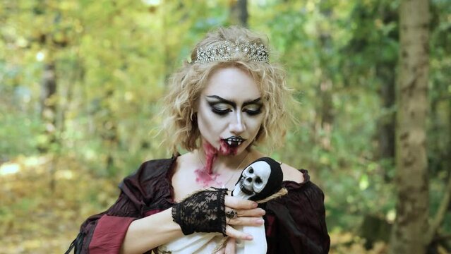 A woman in the form of a vampire or a witch holds a doll in the form of death in her hands. Blood trickles down the vampire's chin. Horizontal video