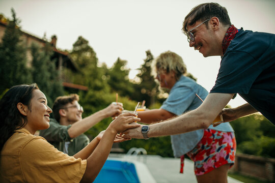 The male host serves juices and drinks to his friends around the pool.