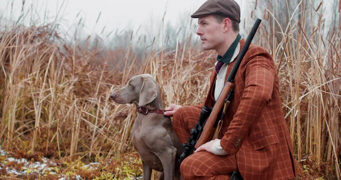 careful hunter and his friend are sitting in an ambush for ducks. Slow motion, man in suit and hata gun with in search of prey in the steppe, pond , lake, field