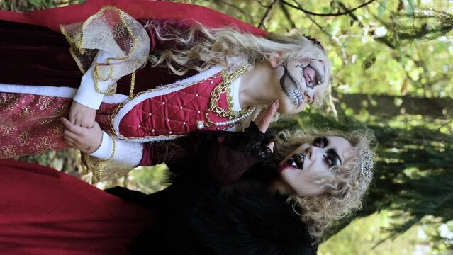 A woman in the form of a vampire or a sorceress poses in the forest with a girl in fairy-tale makeup and medieval dress. Look for Halloween. Vertical video