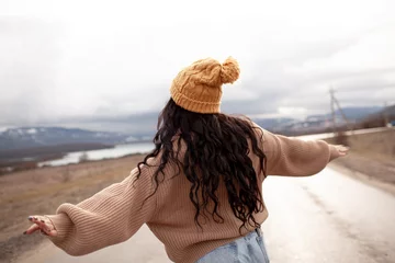 Zelfklevend Fotobehang Beutiful woman is wearing jeans, sweater and hat walking in cold weather along the road        against the background of landscape and nature. A plus size girl is travelling © Вероника Зеленина