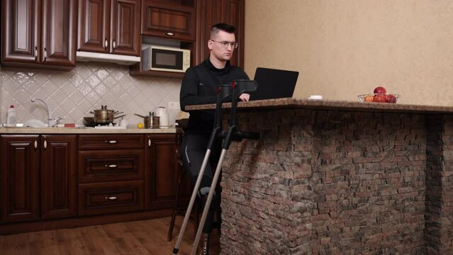 impairment support, Prosthetic leg, wearing glasses. Man with prosthetic leg, wearing glasses, works on laptop with crutches nearby.