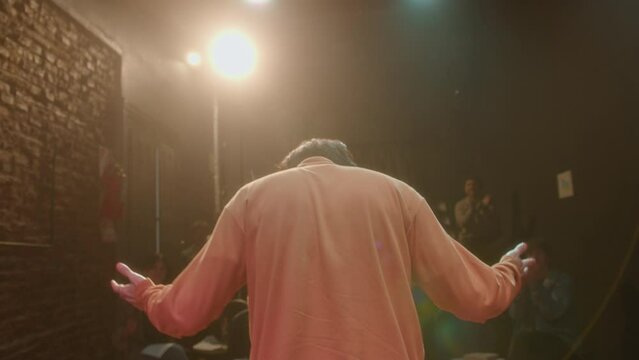 Back view of actor taking a bow in front of applauding audience after giving a solo performance on theater stage
