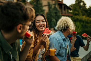 Side view of a smiling diverse group of people eating watermelon and having fun during a backyard party.