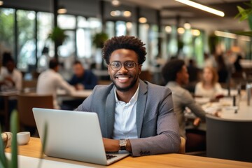 Obraz premium Confident young African businessman sitting at a desk with a group of colleagues in the background working on the laptop computer