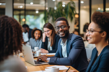 Confident young African businessman sitting at a desk with a group of colleagues in the background working on the laptop computer