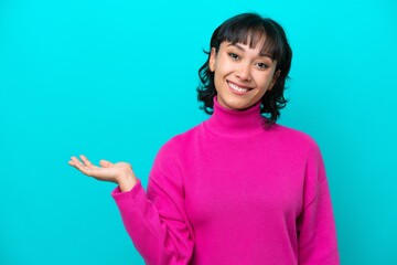 Young Argentinian woman isolated on blue background holding copyspace imaginary on the palm to insert an ad