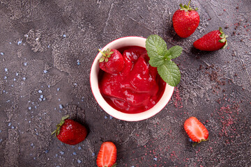 Strawberry sorbet in bowl and fresh berries. Summer refreshing dessert over on dark background.