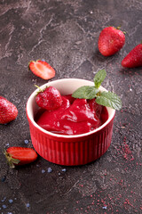 Strawberry sorbet in red bowl and fresh berries. Summer refreshing dessert over on dark background.