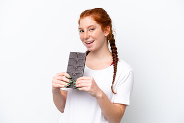 Young reddish woman isolated on white background taking a chocolate tablet and happy