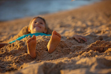 Child, tickling sibling on the beach on the feet with feather, kid cover in sand, smiling, laughing