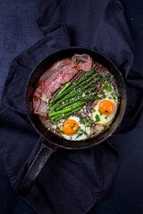 Delicious breakfast lunch branch of fried eggs, bacon, green asparagus, greenery and parmesan cheese on pan.